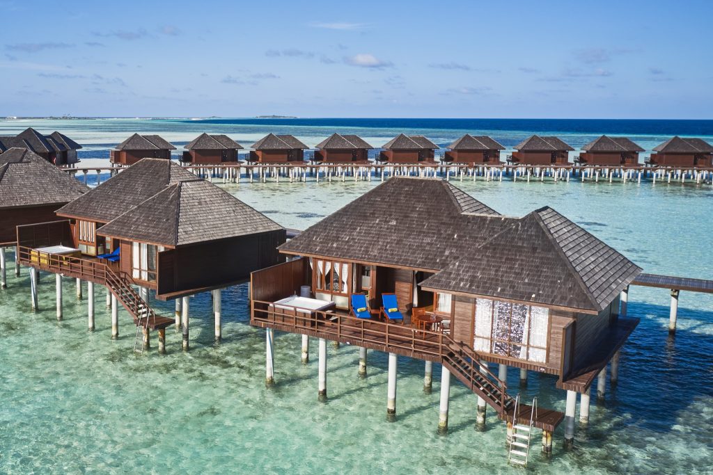 Reihe von Holz-Wasserbungalows mit Schindeldächern und blauen Liegestühlen auf der Terrasse über türkisfarbener Lagune