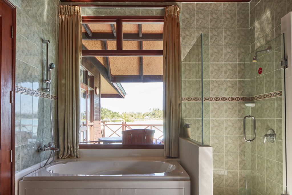 Badezimmer der Water Villa im Sun Siyam Olhuveli mit Badewanne vor großem Fenster und grünlichen Kacheln