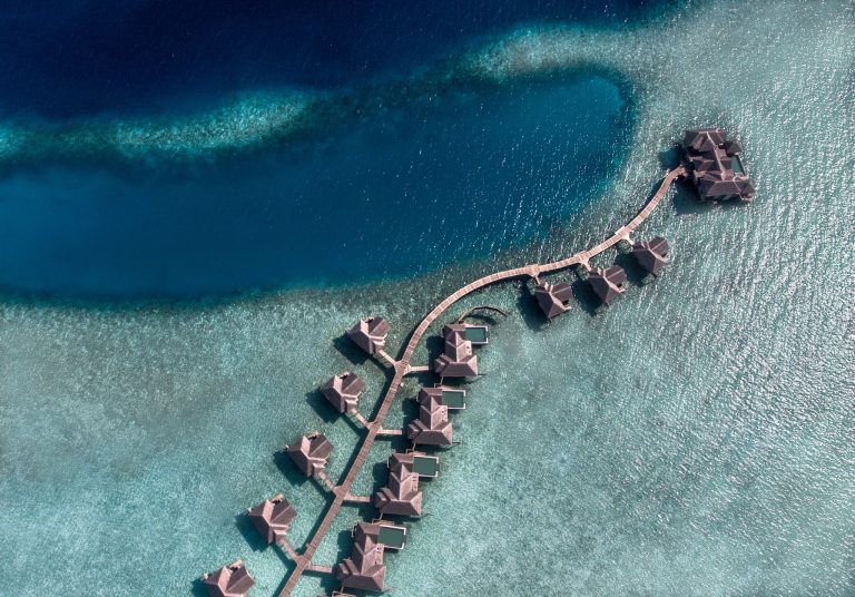 Wasserbungalows mit strohgedeckten Dächern auf Steg über blaugrünem Wasser, Vogelperspektive Vakkaru Maldives