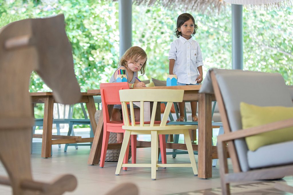 Innenraum im Vakkaru Maldives Kids Club mit Holztisch, bunten Kinderstühlen, Sofa und großem Fenster