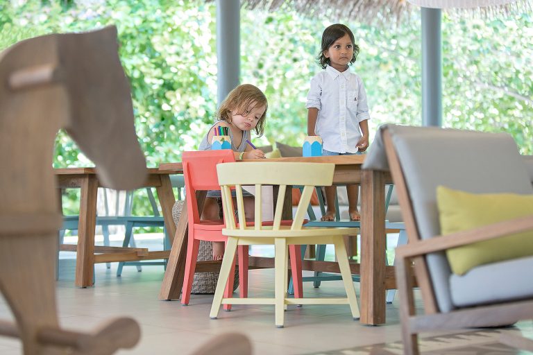 Innenraum im Vakkaru Maldives Kids Club mit Holztisch, bunten Kinderstühlen, Sofa und großem Fenster