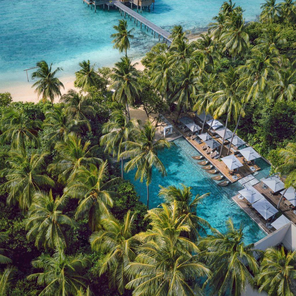 Luftaufnahme des Vakkaru Maldives Poolbereichs mit Holzterrasse, Liegestühlen, Palmen und angrenzendem Sandstrand