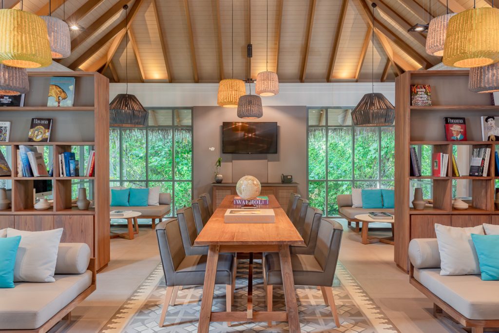 Offener Loungebereich im Vakkaru Maldives mit langem Holztisch, gepolsterten Stühlen und großen Fenstern zur grünen.