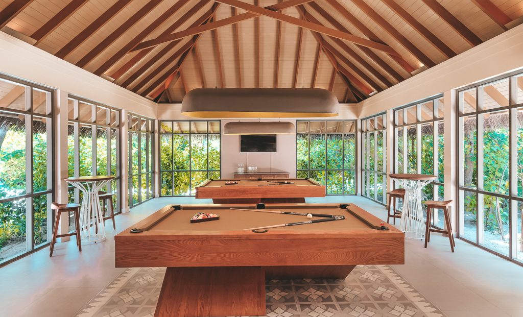 Modernes Billardzimmer mit zwei Holztischen, großen Fenstern, Holzbalkendecke und gemustertem Boden im Vakkaru Maldives