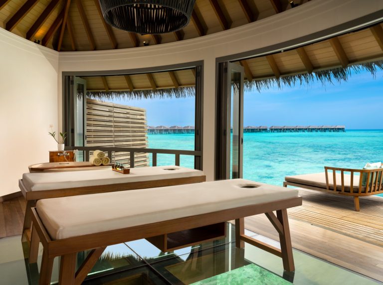 Wellness Spa Bereich mit zwei Massageliegen auf Glasboden und Blick auf Meer und Wasserbungalows