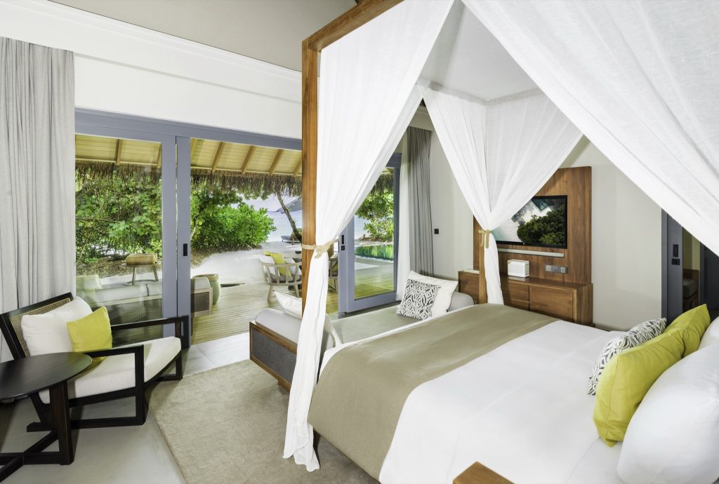 Zimmer Beach Pool Villa mit Himmelbett, Holzmöbel, Glas-Schiebetür zur Terrasse und Meerblick im Vakkaru Maldives