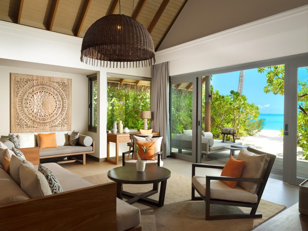 Hotel-Lounge der One Bedroom Beach Pool Residence mit Holzmöbeln, großen Glas-Schiebetüren und Blick auf Strand und Meer