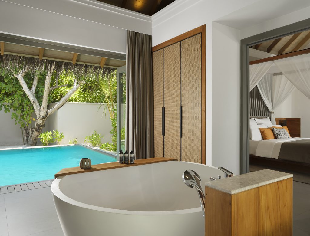 Hotelzimmer mit freistehender Badewanne, Pool mit türkisblauem Wasser und Blick auf Schlafzimmer mit Baldachin