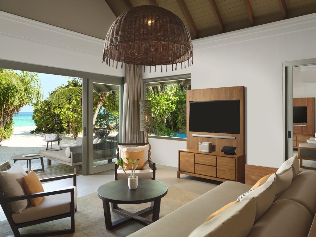 Wohnzimmer der One Bedroom Deluxe Beach Pool Residence mit Glasfenstern, Holzmöbeln und Blick auf Strand