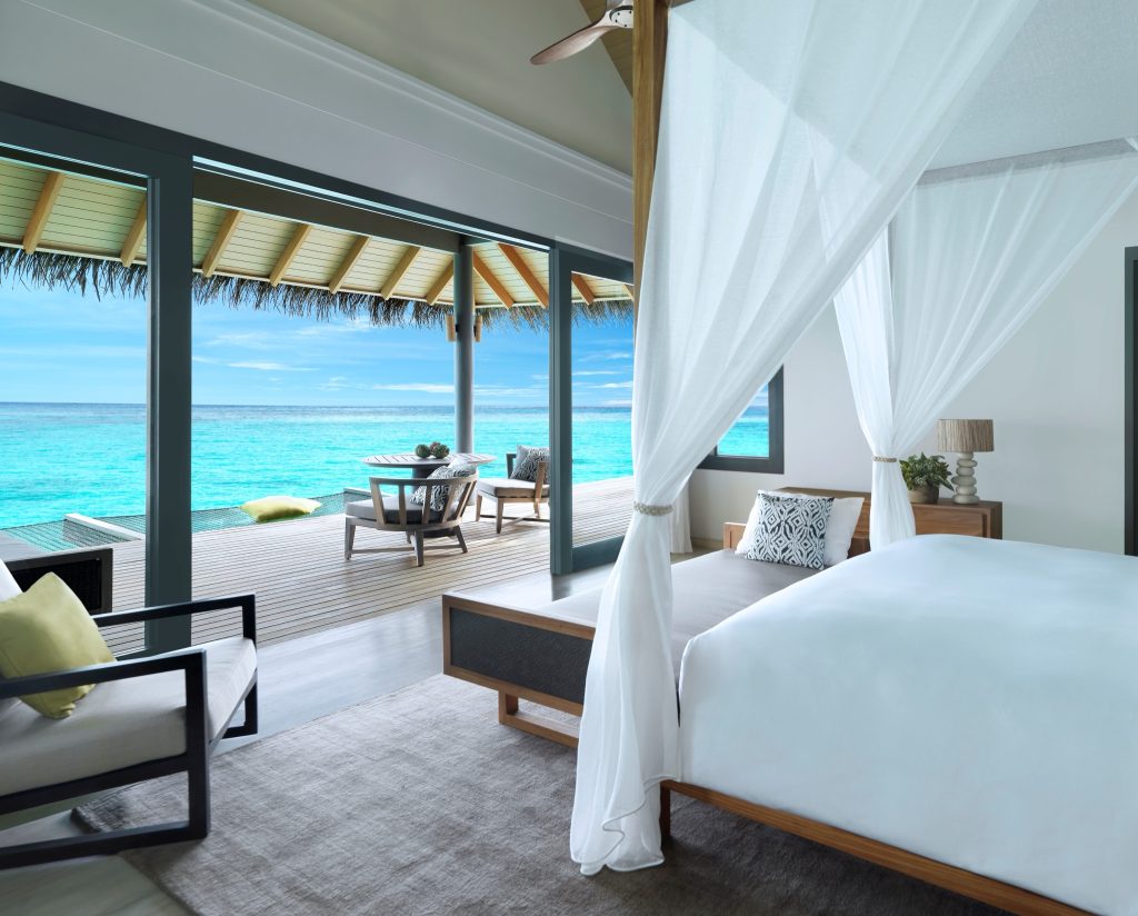 Zimmer der Overwater Villa im Vakkaru Maldives mit weißem Baldachinbett und Meerblick von der Terrasse