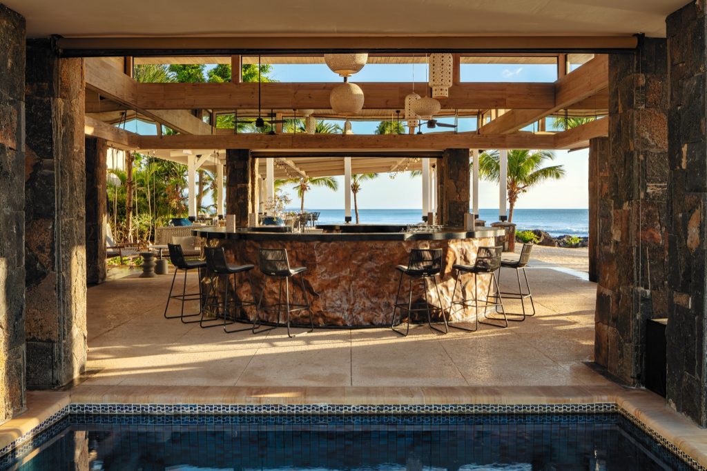 Offene Bar Mystique mit gemusterten Steinwänden, hohen schwarzen Hockern und Blick auf Meer und Pool