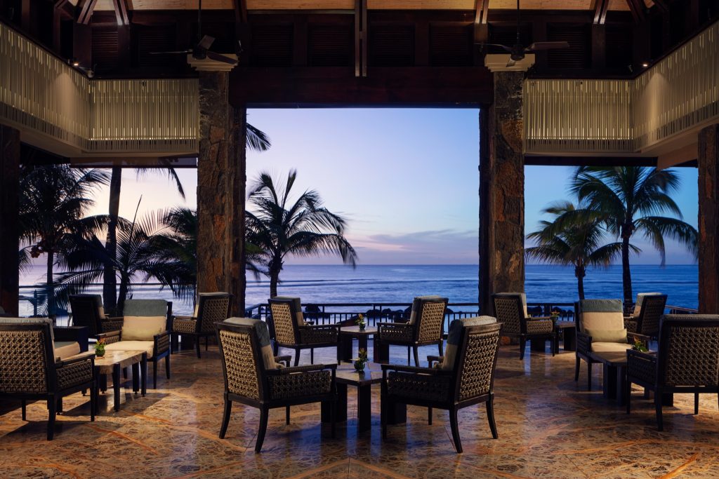 Offene Bar Lounge mit Holzsesseln und Marmorfußboden, Steinpfeilern und Meerblick bei Dämmerung im Bar Retreat