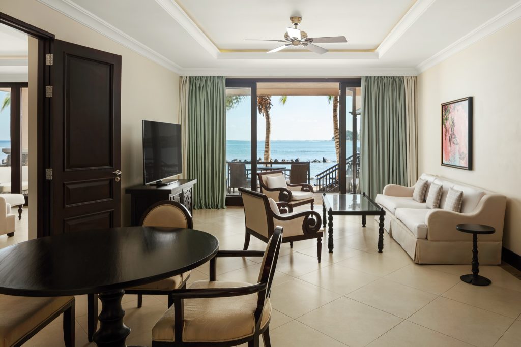 Zimmerbereich der Banyan Suite mit dunkelbraunem Holztisch, beiger Couch und Balkon mit Meerblick