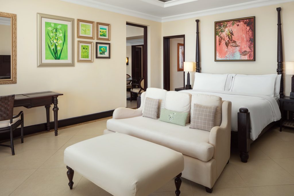 Banyan Suite Zimmer mit großem Doppelbett, beigem Sofa, Holz- und Rattanmöbeln sowie gerahmten grünen Kunstwerken