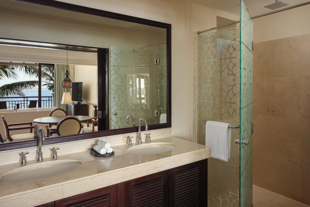 Badezimmer der Beachfront Suite mit großem Spiegel, hellem Marmorwaschtisch und verzierter Glasdusche