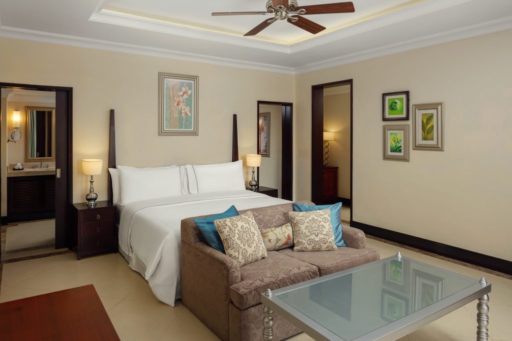 Junior Suite Zimmer mit Doppelbett, Couch, Glastisch, warmen beigen Wänden und Deckenventilator