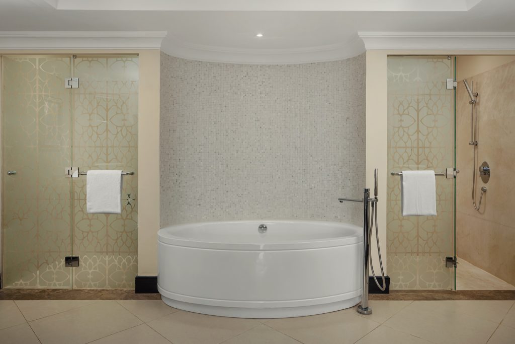 Badezimmer in der Junior Suite mit freistehender ovaler Badewanne und zwei gläsernen Duschen mit Mosaikfliesenwand
