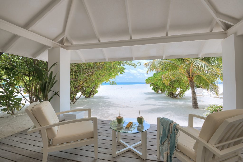 Überdachte Terrasse im Diamonds Thudufushi Maldives Resort & Spa mit weißen Sesseln und Blick auf Strand und Meer