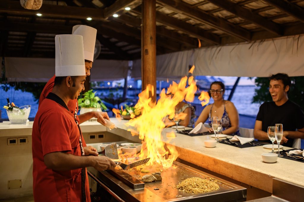 Zwei Köche in roten Uniformen und weißen Mützen arbeiten an einer Teppanyaki-Platte vor