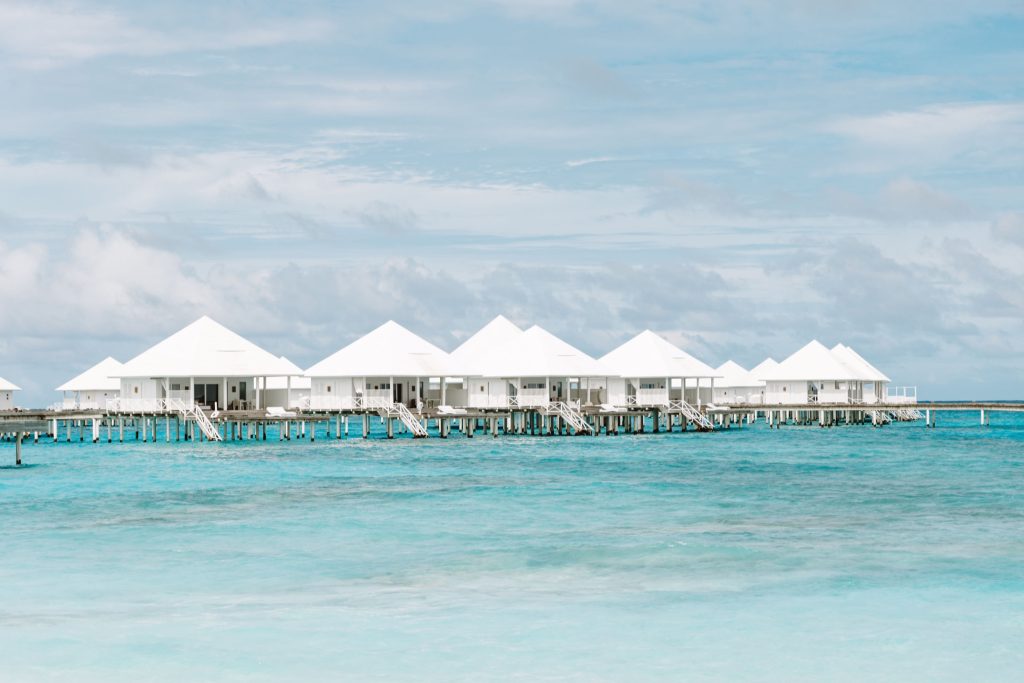 Weiße Holzbungalows auf Stelzen über türkisfarbenem Meer unter blauem Himmel im Diamonds Thudufushi Maldives Resort & Spa