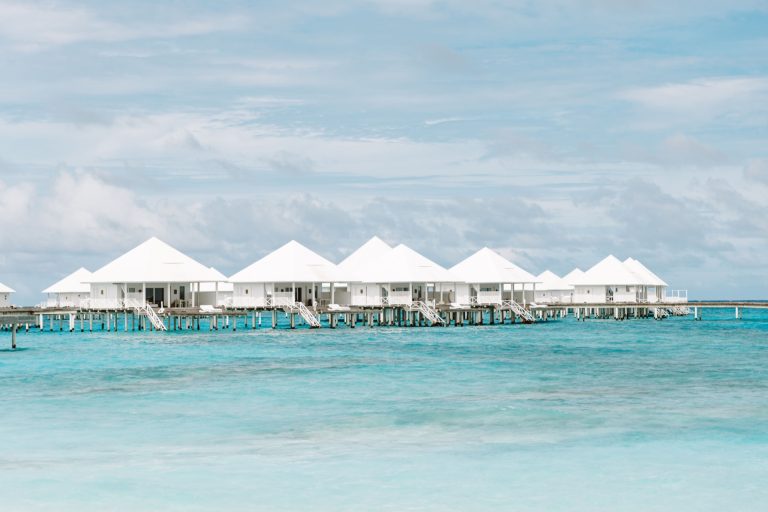 Weiße Holzbungalows auf Stelzen über türkisfarbenem Meer unter blauem Himmel im Diamonds Thudufushi Maldives Resort & Spa