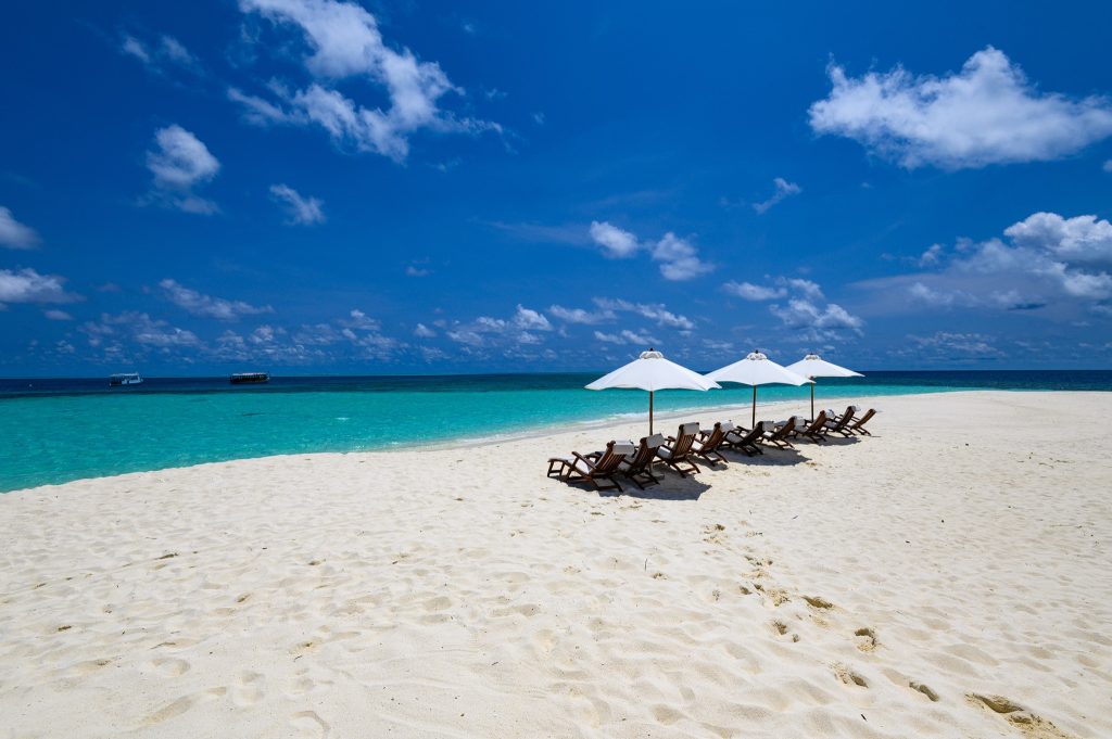 Strandbereich mit weißen Sonnenschirmen und Sonnenliegen vor türkisblauem Ozean bei klarem Himmel