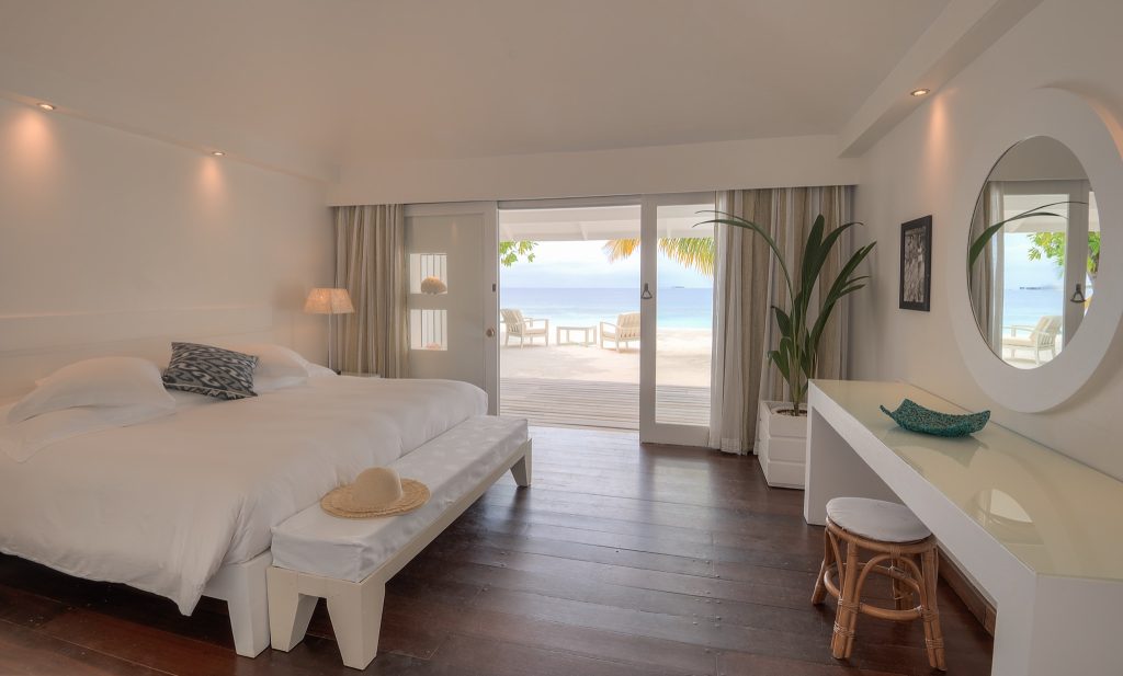 Modernes Hotelzimmer mit großem Bett, Strohhut auf Bank, Schreibtisch und Terrasse mit Meerblick