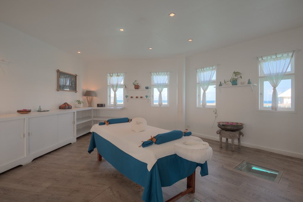 Wellnessraum mit zentralem Massagetisch, weißen und blauen Stoffen, großen Fenstern und hellem Holzboden im Diamonds.