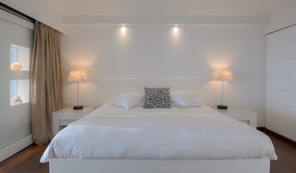 Modernes Hotelzimmer mit großem Bett, weißen Kissen, Stehlampen und Holzboden im Diamonds Thudufushi Maldives Resort & Spa