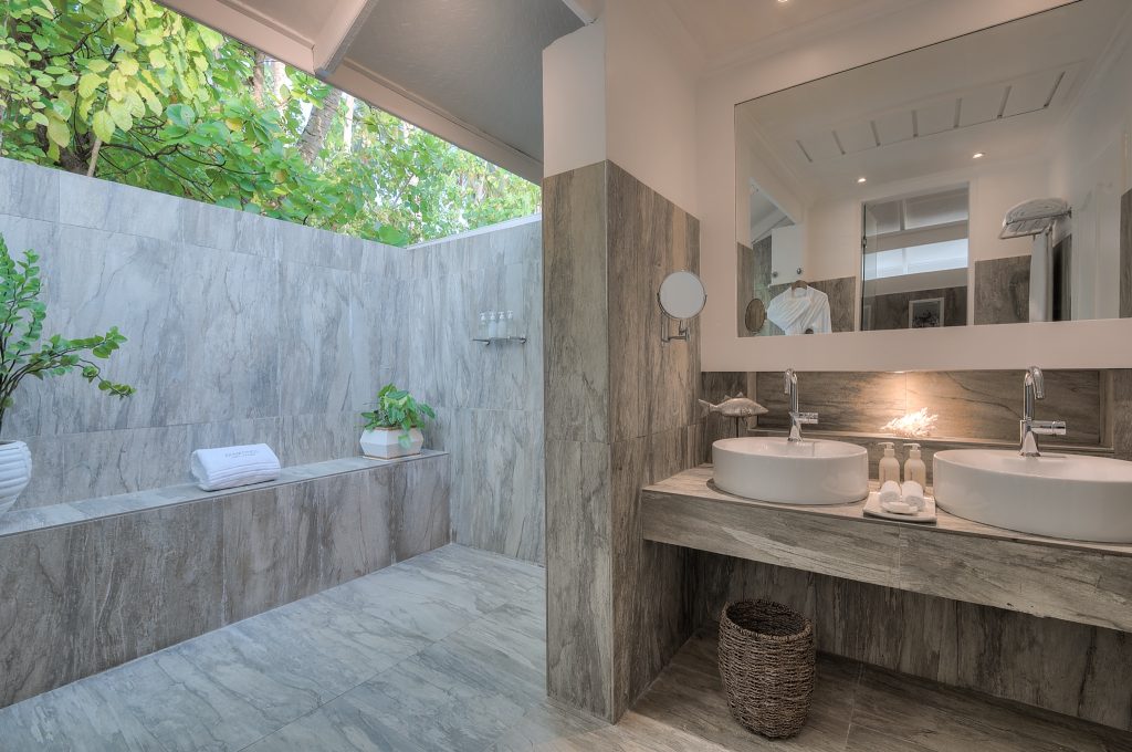 Modernes Badezimmer mit zwei runden Waschbecken, halb offener Dusche, Steinwänden und Pflanzen auf den