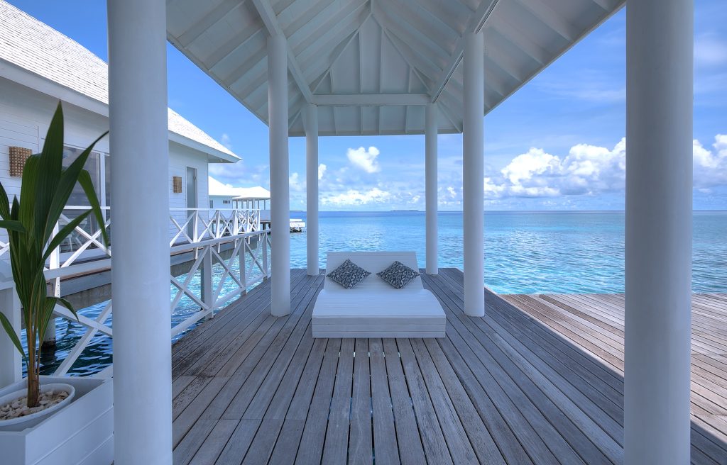 Terrasse mit weißem Tagesbett und schwarzen Kissen, weißen Säulen und Blick auf das offene Meer