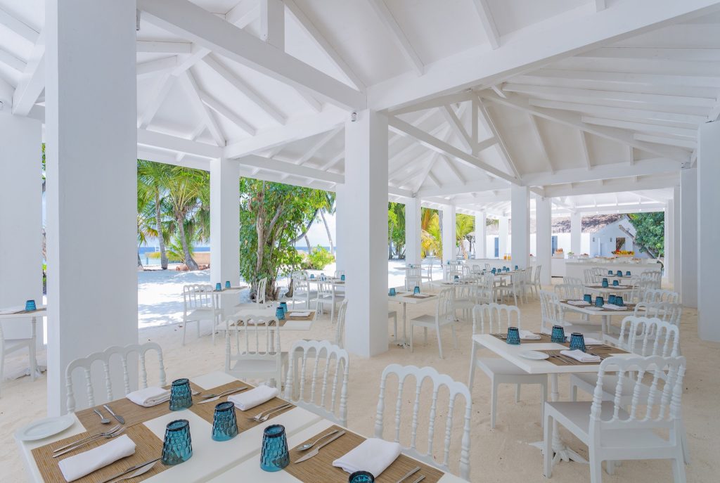 Offener Restaurantbereich im Sandies Bathala Maldives mit weißen Holztischen und blauer Tischdekoration auf sandigem Boden