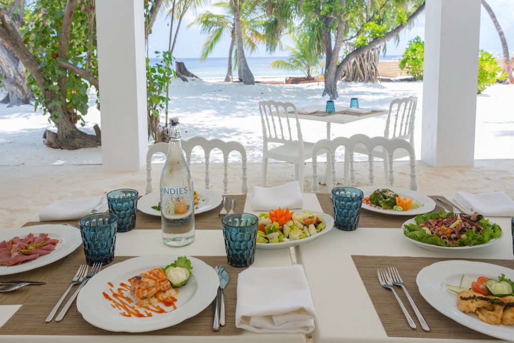 Freiluftrestaurant Tisch mit Tellern, blau getönten Gläsern, weißen Servietten und Meerblick auf den