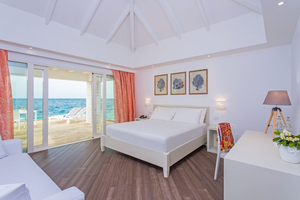 Hotelzimmer mit großem weißen Bett, Sofa, Schreibtisch, Holzfußboden und Terrasse mit Meerblick