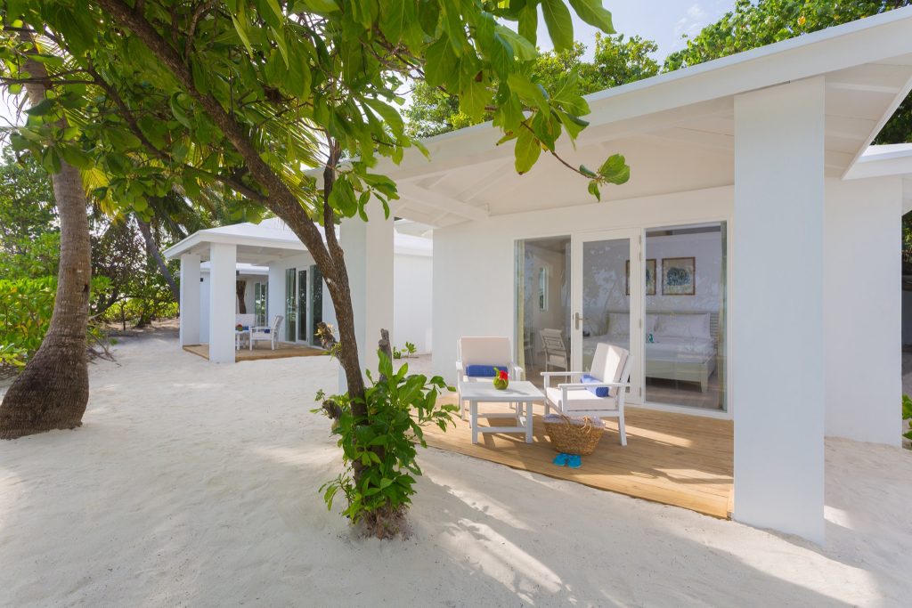 Modernes Beach Villa Bungalow mit weißen Wänden, großen Glasfronten und Terrasse mit Gartenmöbeln am Sandstrand