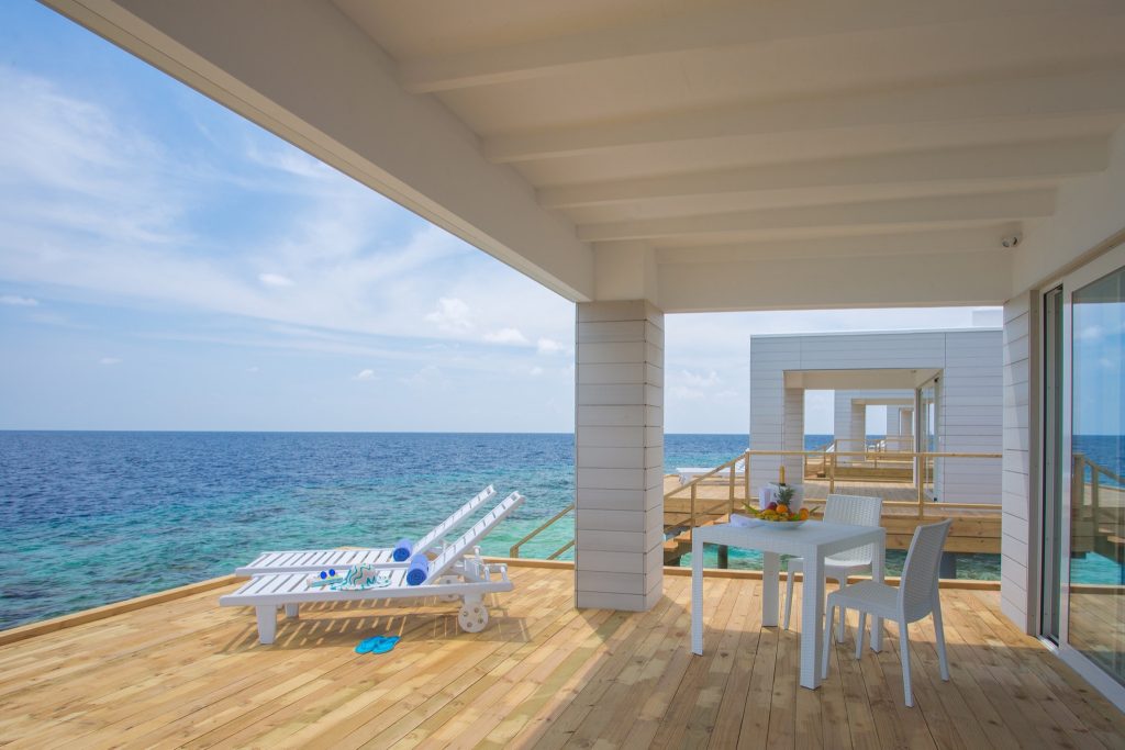 Terrasse der Water Villa im Sandies Bathala Maldives mit weißen Liegestühlen, Holzboden und Blick auf das blaue Meer