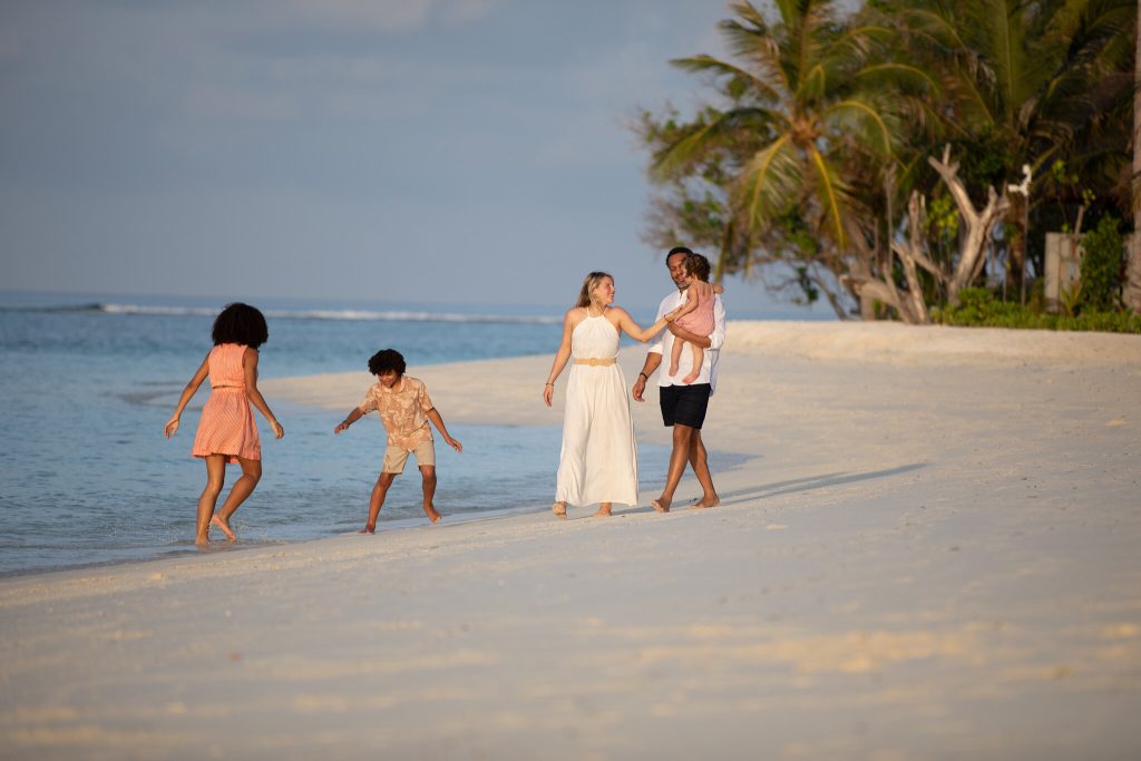 Familie mit Kindern am Strand von Six Senses Kanuhura auf den Malediven bei Sonnenuntergang mit Palmen im Hintergrund