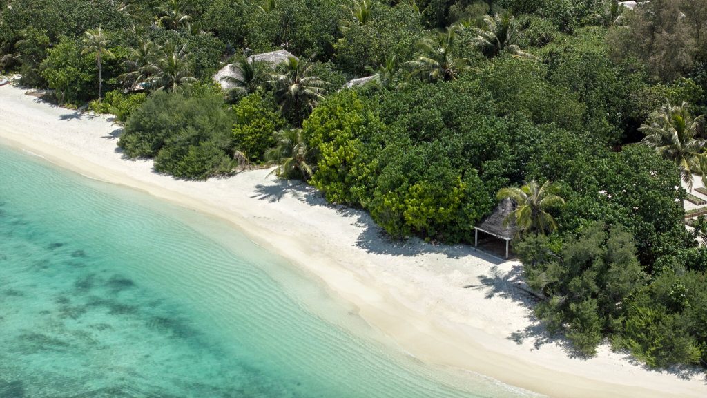 Luftaufnahme eines Strandes mit hellen Sand, tropischem Wald und strohgedeckten Hütten am Meer