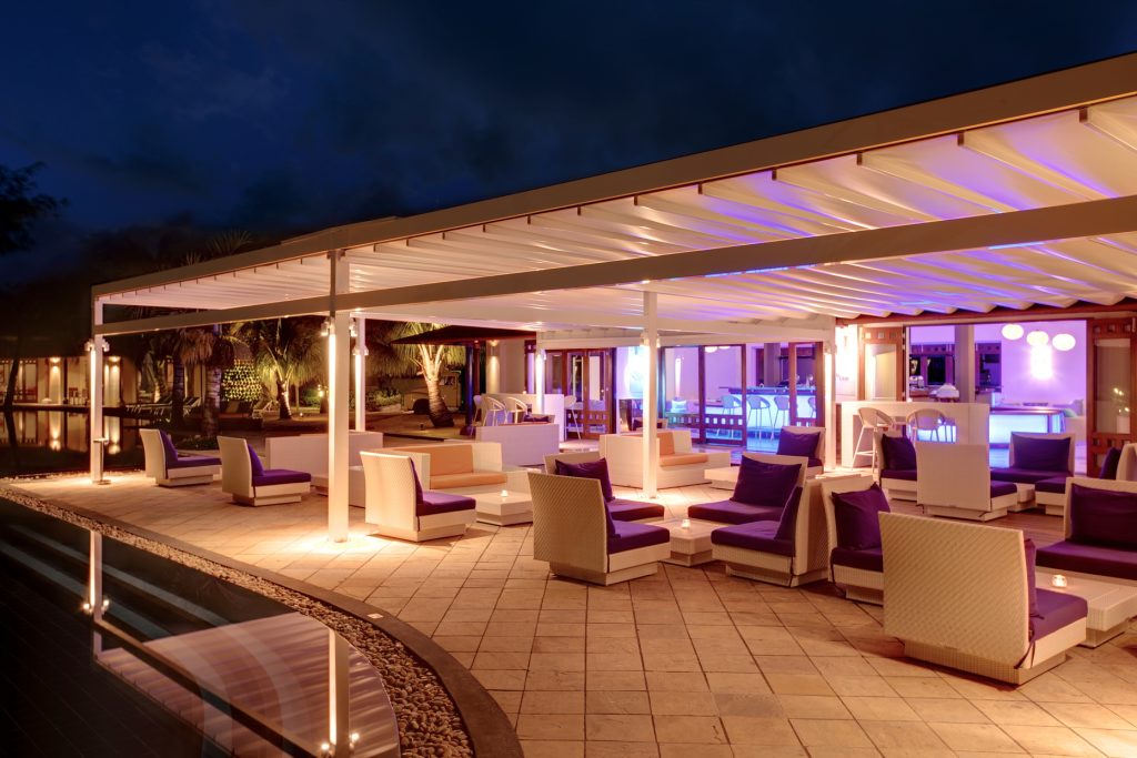 Beleuchtete Terrasse der Bar B Bar im Tamassa Bel Ombre mit weißen Rattanmöbeln, violetten Kissen