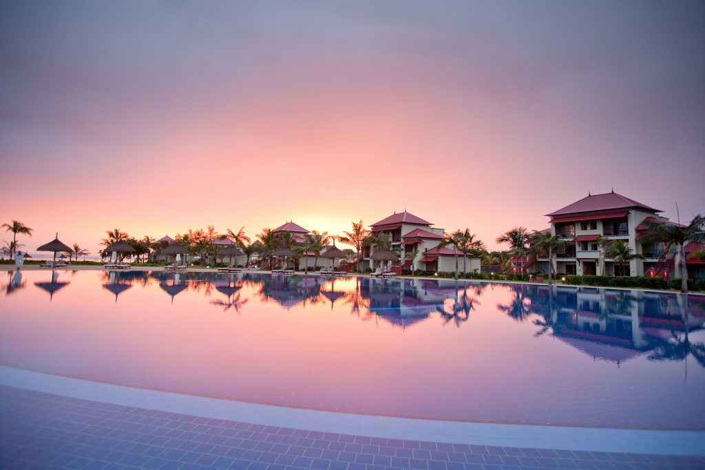 Großer Pool mit Reflexion von Palmen und roten Dächern des Hotels Tamassa Bel Ombre auf Mauritius