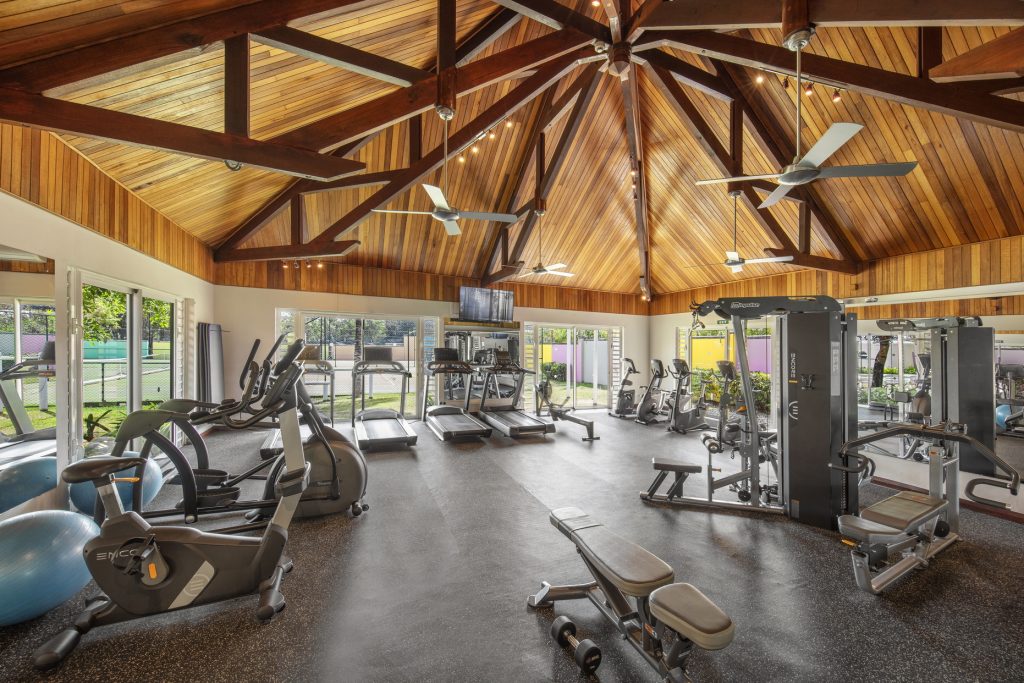 Moderner Fitnessraum mit Laufbändern, Fahrradergometern und Kraftmaschinen, Holzdach und großen Fenstern