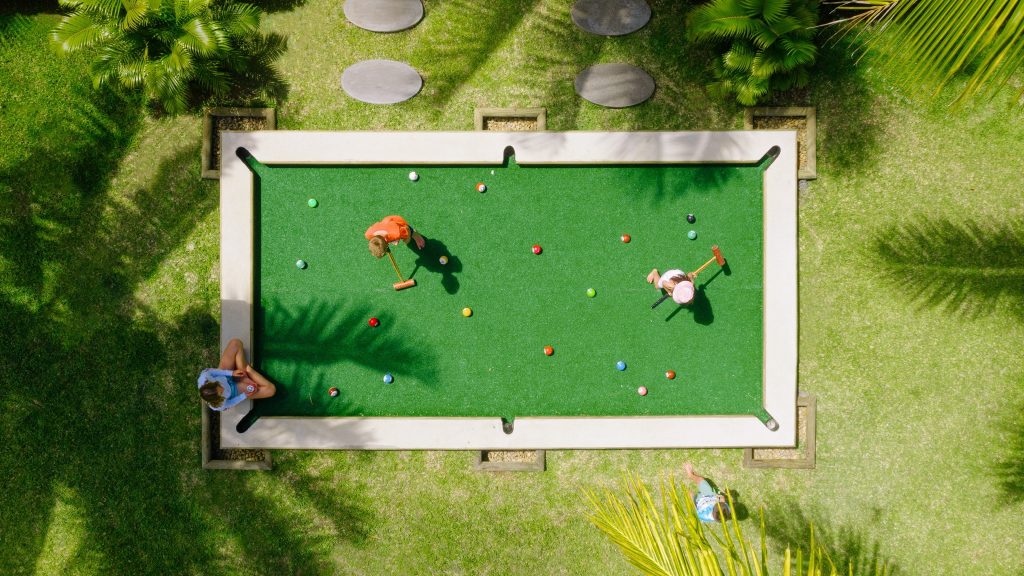 Outdoor Billardtisch mit bunten Kugeln auf grünem Rasen, umgeben von Palmen, bei hellem Tageslicht in Mauritius