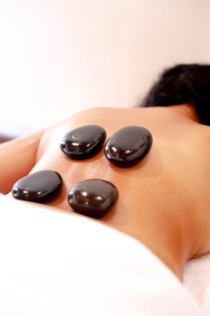 Person erhält Hot-Stone-Massage mit vier dunklen Steinen auf Rücken in Spa-Umgebung