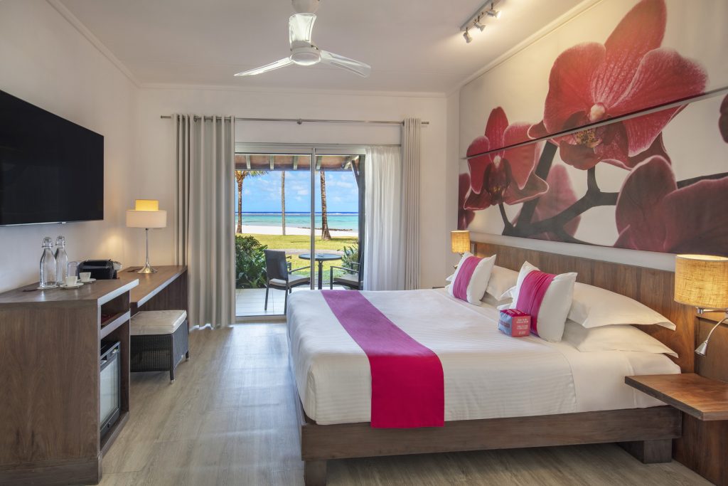 Hotelzimmer im Tamassa Bel Ombre Beach Room mit großem Bett, Flachbildfernseher, Schreibtisch und Balkon mit Meerblick