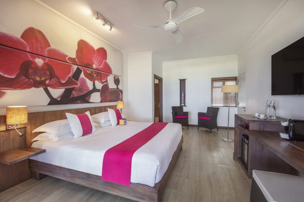 Modernes Beach Room Zimmer im Tamassa Bel Ombre mit Holzbett, weißen Wänden und pinken Kissen