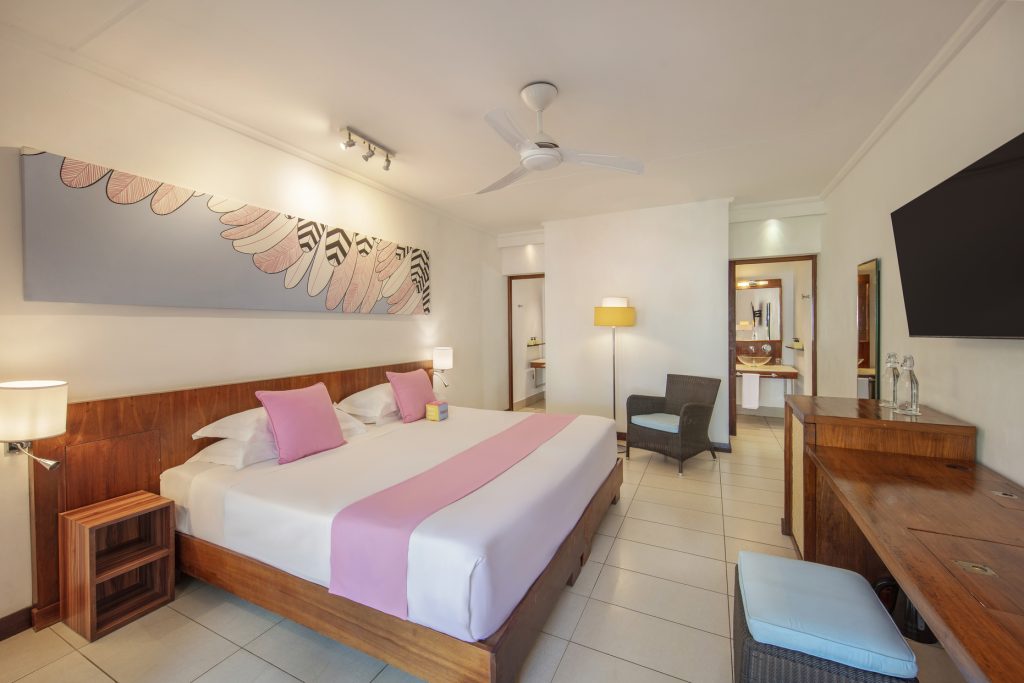 Helles Superior Room Zimmer im Tamassa Bel Ombre mit Doppelbett, rosafarbenen Kissen, Flachbildfernseher und Holzmöbeln