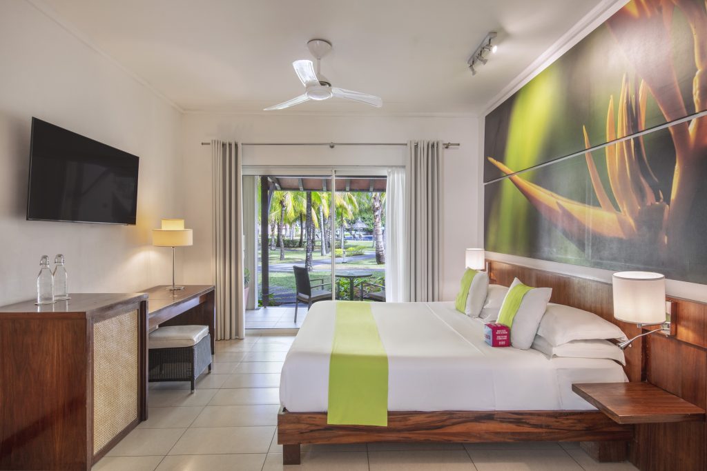 Modernes Hotelzimmer im Tamassa Bel Ombre mit großem Bett, limonengrünen Akzenten und Blick auf Terrasse mit Palmen