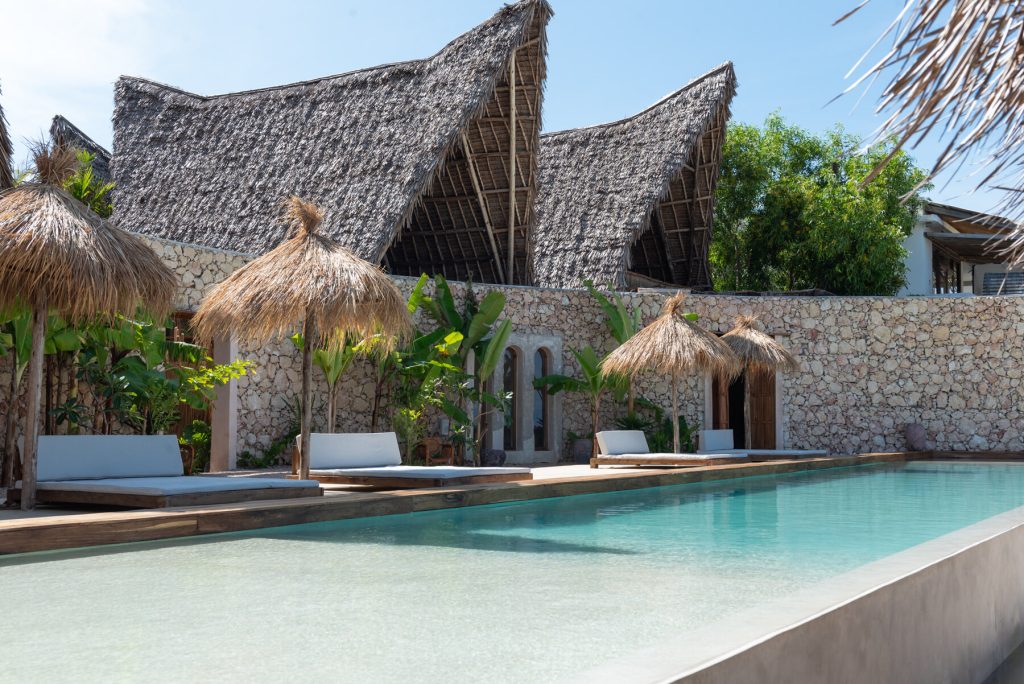 Außenpool von Be Zanzibar mit Holzliegen, Strohdach-Sonnenschirmen und natürlichem Steingemäuer