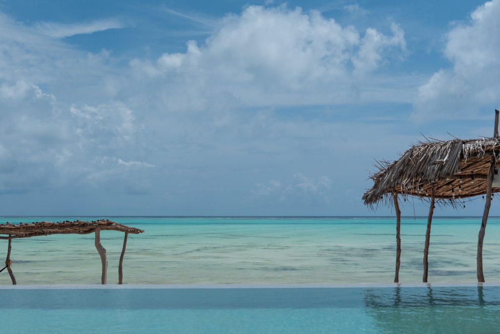 Infinity-Pool mit türkisfarbenem Ozean und zwei Strohdächern aus Holz auf Sansibar