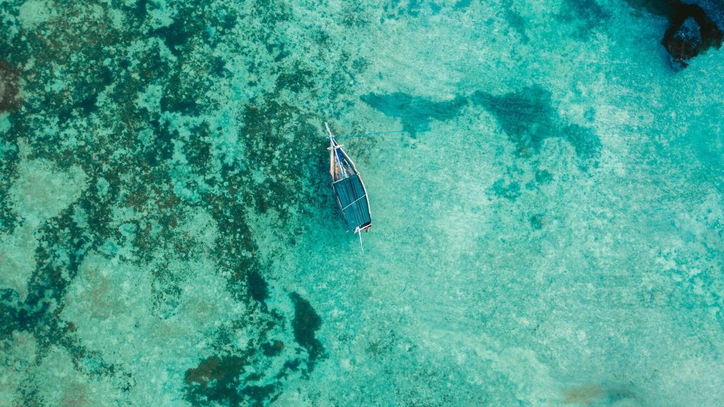 Kleines Holzboot auf klarem türkisfarbenem Wasser über Korallenriff mit grünen Algen